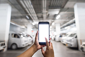 Image of a person's hands using a mobile device in an underground parking garage with cars visibly in parking spots in background.