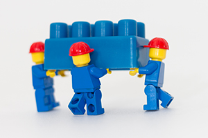 Image of three lego persons holding up large lego block together