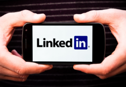 A photograph of two hands holding a cellphone whose screen is displaying the LinkedIn logo 