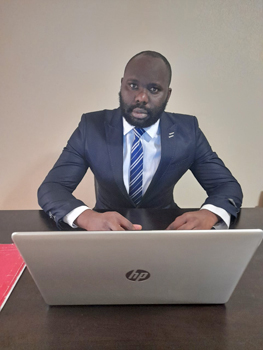 A photograph of graduate student Cyril Akwo sitting at a desk in front of his laptop computer.