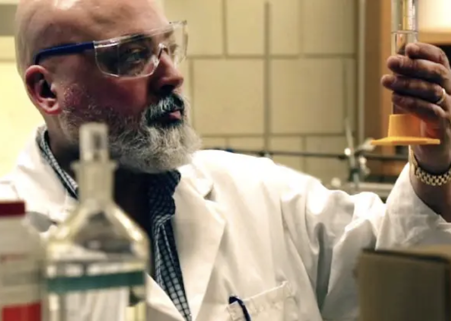 Image of Dr. Monteiro looking at a beaker while wearing personal protective equipment in a lab